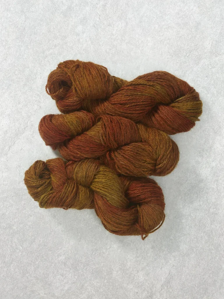 Twisted skeins of semi-solid wool yarn in rich amber gold with warm orange and earthy brown undertones
