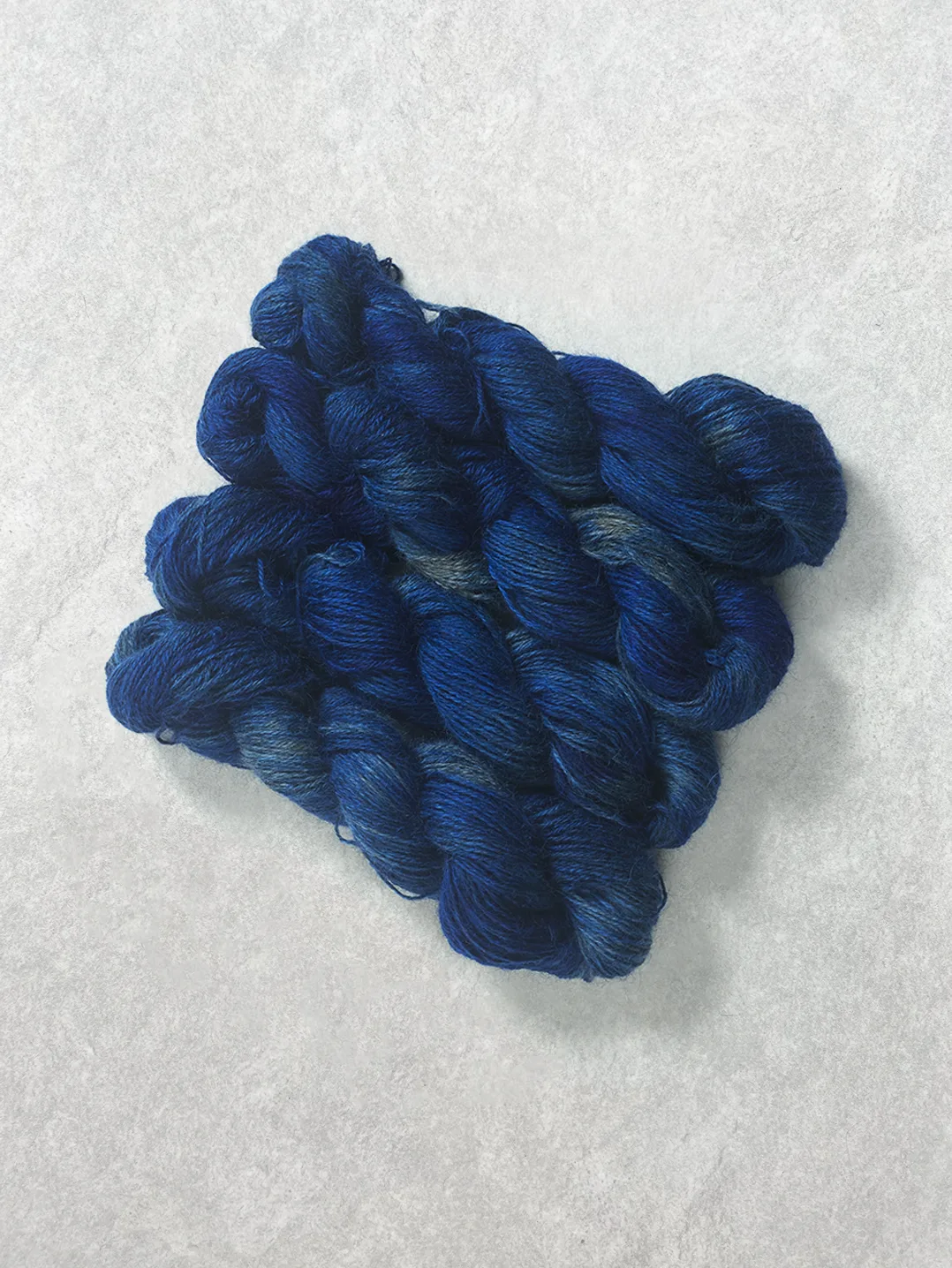 Twisted skeins of hand-dyed wool yarn in rich tonal shades of deep blue and indigo on a textured background