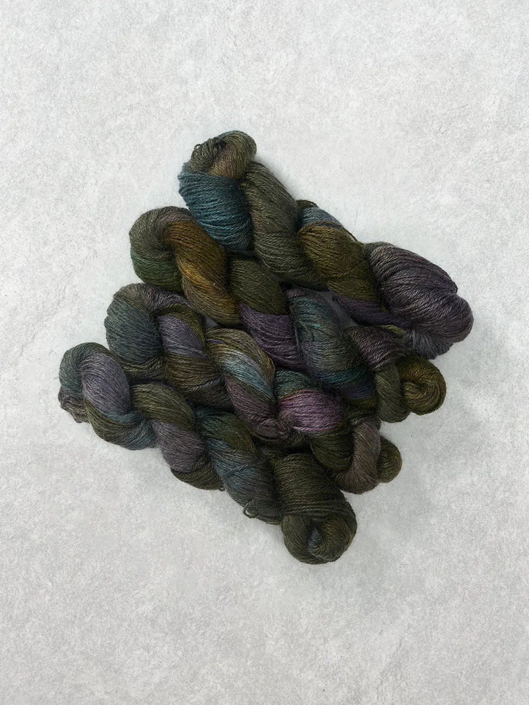 Twisted skeins of hand-dyed wool yarn featuring variegated shades of deep purple forest green and dark teal