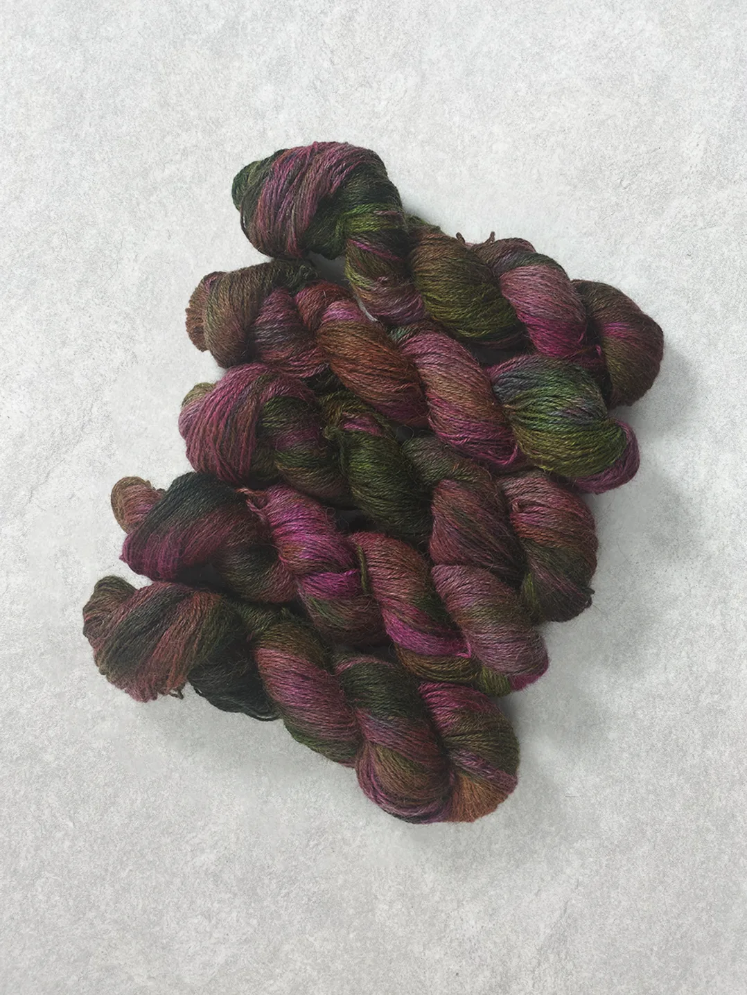 Twisted skeins of hand-dyed wool yarn in variegated shades of bright fuchsia pink and forest green on a textured background