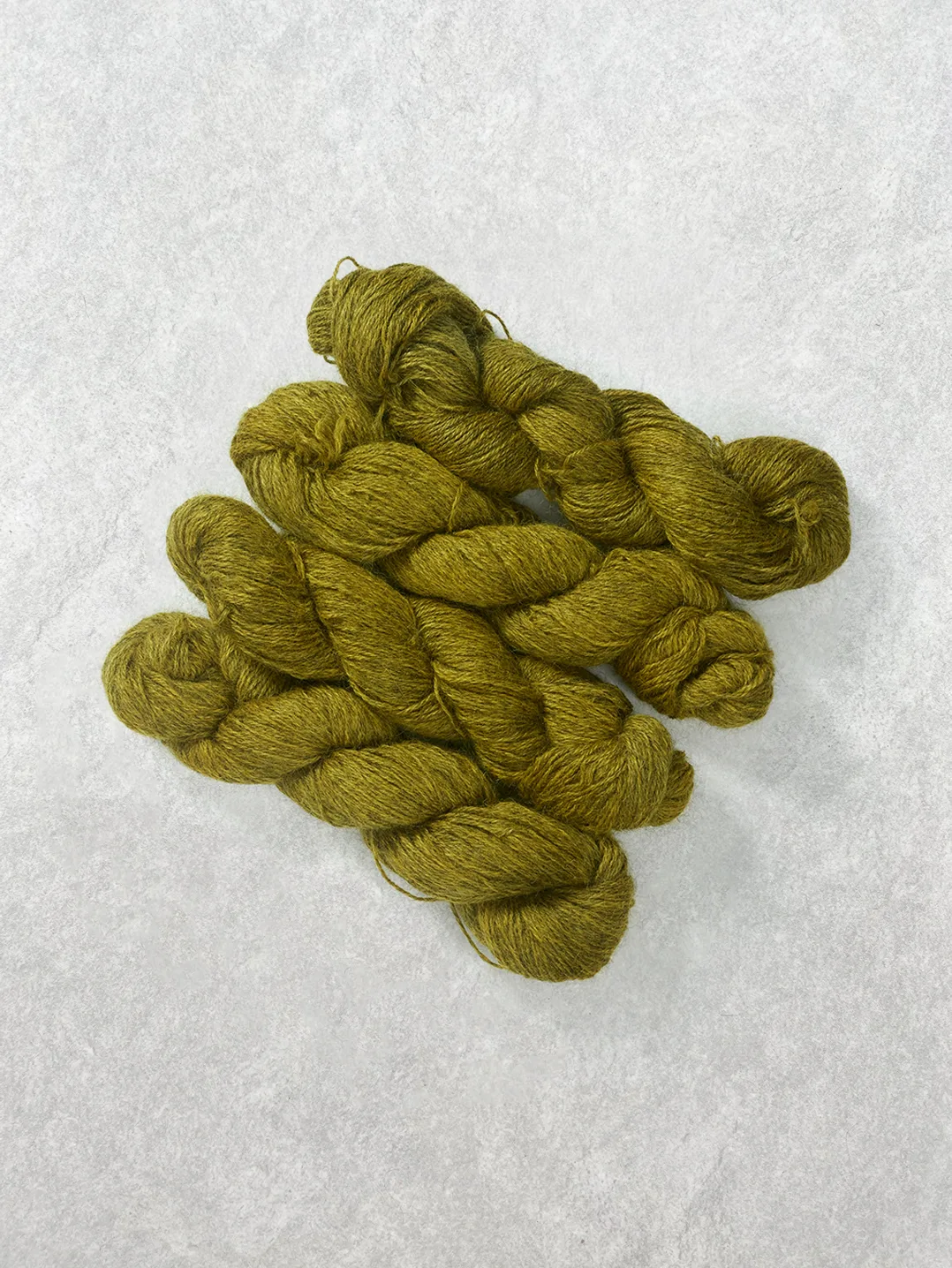 Twisted skeins of semi-solid wool yarn in a rich mustard yellow and ochre shade on a light textured background