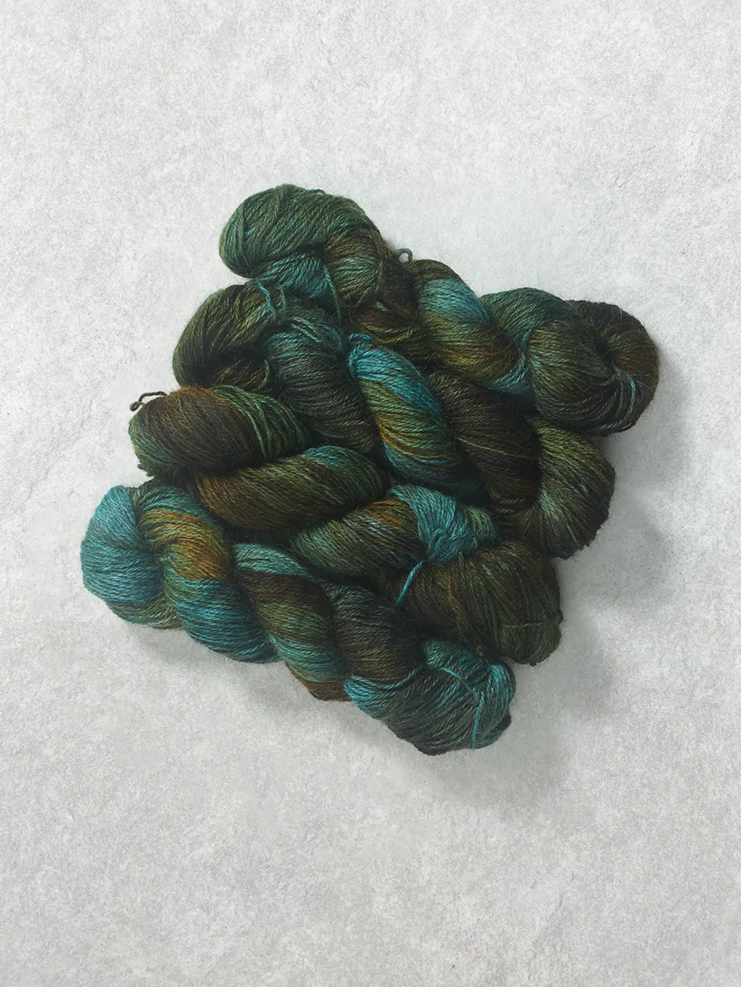 Twisted skeins of hand-dyed wool yarn featuring variegated shades of dark chocolate brown and vibrant mint teal green