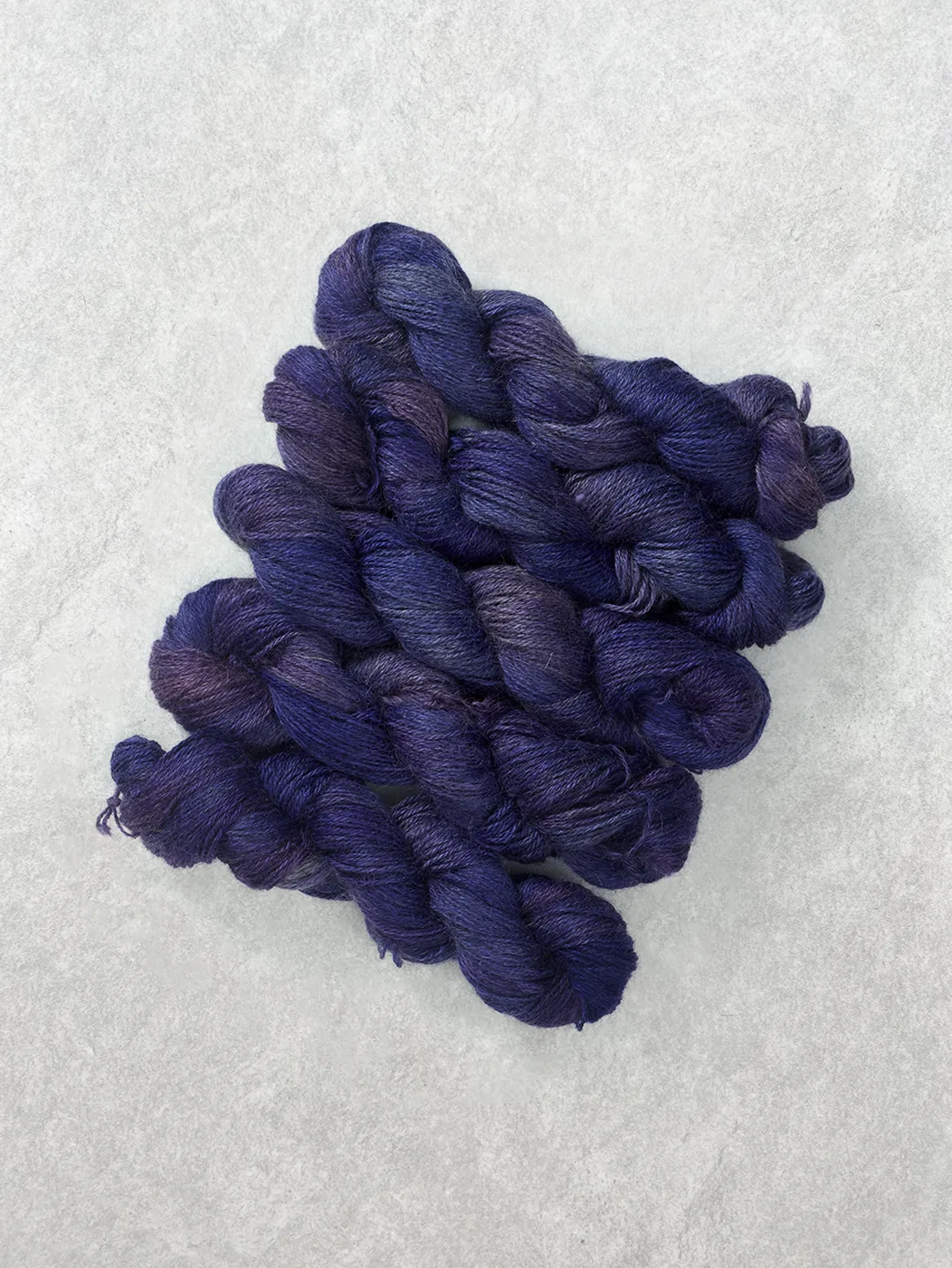 Twisted skeins of hand-dyed wool yarn in rich tonal shades of deep purple and violet on a light textured background