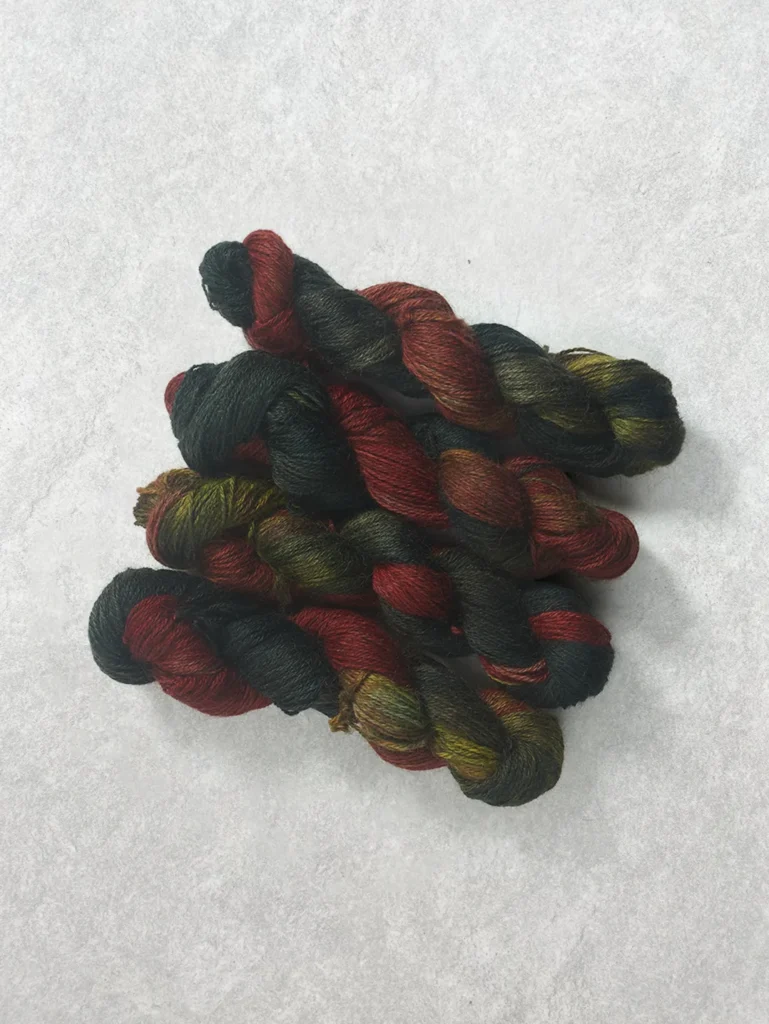 Twisted skeins of hand-dyed wool yarn featuring high contrast variegated shades of deep spruce green and bright firecracker red